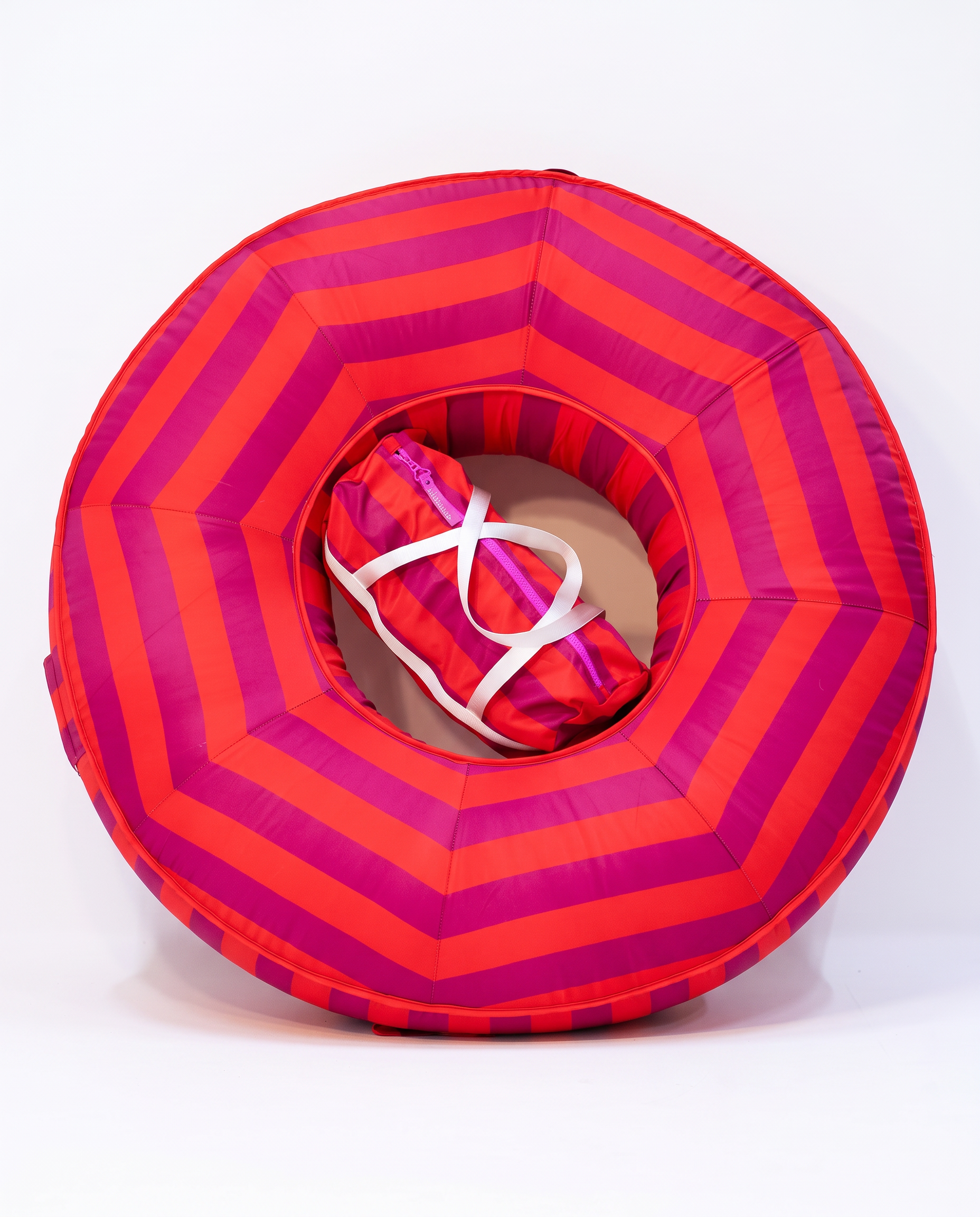 A red and fuchsia striped inflatable pool float with a matching striped inner bag secured by a white strap, photographed on a clean white background.